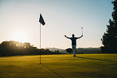 A golfer is celebrating a hole at sunset on the green