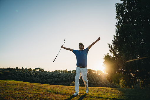 Shot of male golfer with golf club at course. Young man holding a golf club and looking away on a sunny day.