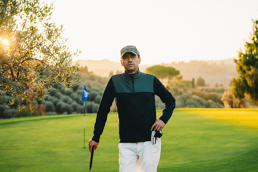 Portrait of a golfer on the golf course at sunset. He's standing near the green.