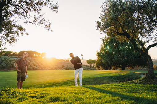 Golf, back and hobby with a sports man swinging a club on a field or course for recreation and fun. Golfing, grass and stroke training with a male golfer playing a game on a course during summer