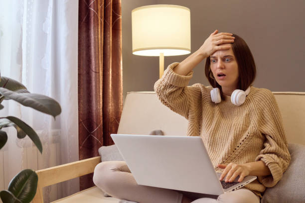 istock Despair woman in knitted sweater using laptop sitting on couch at home working remotely making mistake in report or digital project showing facepalm gesture. 1805757596