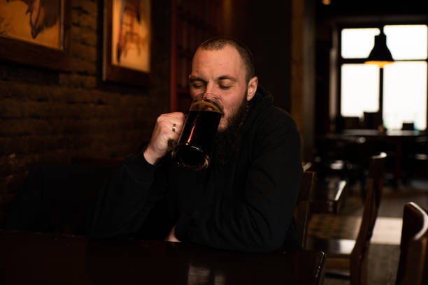 istock bearded man holds glass of beer while sitting in pub. Beer time. Alcohol drinks 1805758696