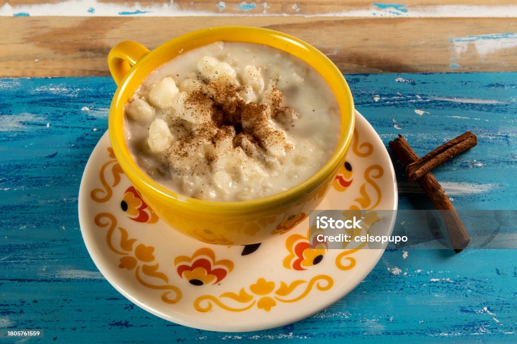 cup of canjica, typical food consumed in the Brazilian Festa Juninas Typical Brazilian sweet dessert, Canjica. White corn porridge with cinnamon and coconut. Consumed at June festivals (festa Junina) on a rustic blue table Bowl Stock Photo