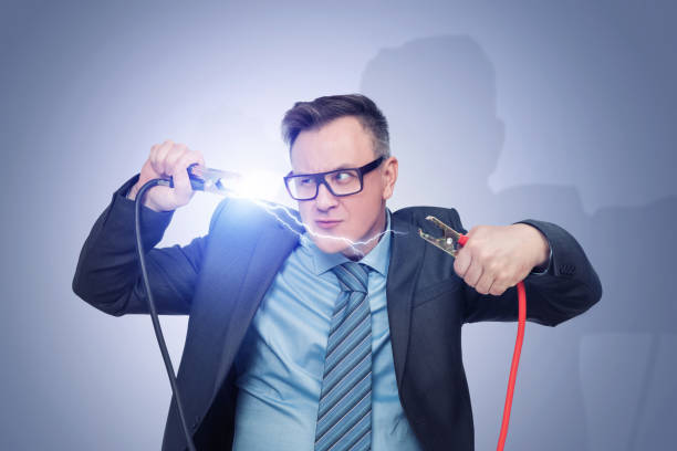istock A man in glasses, suit and tie holds two wires with clips in his hands between which an electric discharge occurs 1805771936