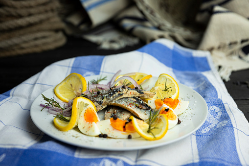 Herring fish fillets with eggs, herbs, onion and lemon on a white plate in the kitchen