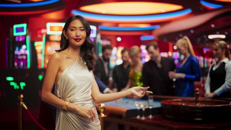 Portrait of a Beautiful Young Asian Woman Wearing an Elegant Silver Dress, Standing in a Modeling Pose and Gesturing at an Empty Space for Your Company Logo or Advertising Campaign Call to Action