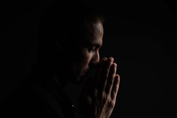 istock Man with clasped hands praying on black background 1805780197