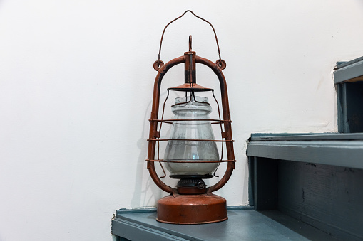 Vintage red kerosene lamp stands on green wooden stairs in front of a white wall, close up photo with selective soft focus