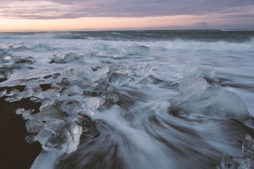 A tranquil beach setting with vast amounts of chunks of ice and water scattered across the shoreline
