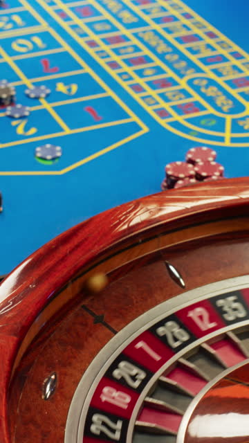 Vertical Screen: Group of Rich Men and Women Gathered Around a Roulette Table at a Modern Casino. Cinematic Close Up Footage of Gambler Hands Placing Bets while the Ball Spinning in a Roulette Wheel