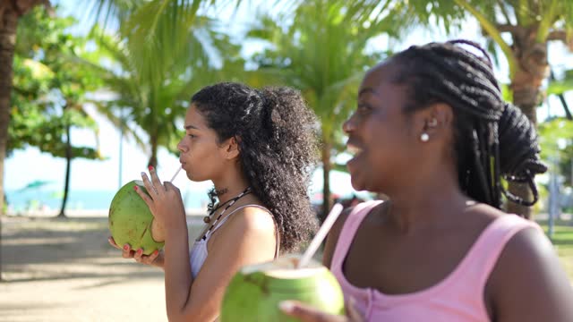 Friends talking and drinking coconut water while walking at the beach