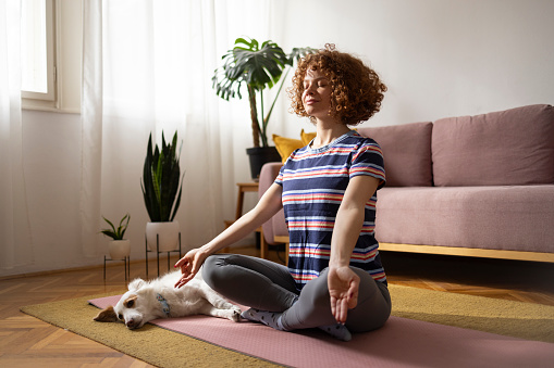 Curly haired woman relaxing yoga routine at home with her pet