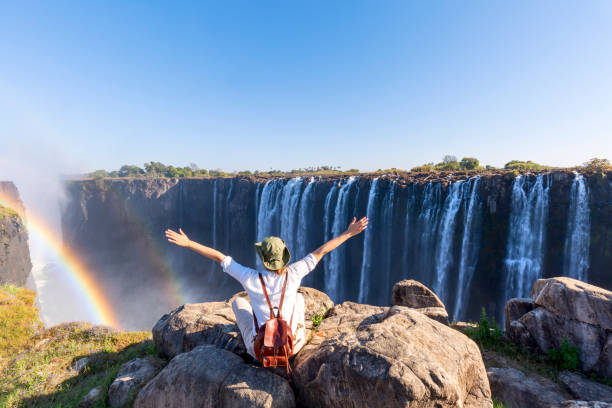 Woman sitting on the top of a rock enjoying the Victoria Falls -  Zimbabwe stock photo