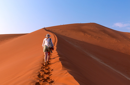 ourist walking on the sand dunes at Sossusvlei, Namib desert, Namib Naukluft National Park, Namibia. Traveling people, adventure and vacations in Africa.