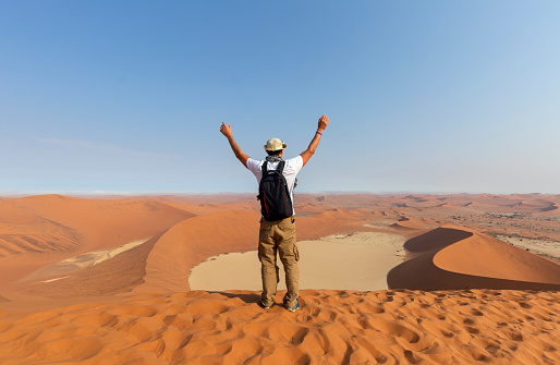 Happy male tourist with open arms on sand dunes in the Africa desert, Namibia