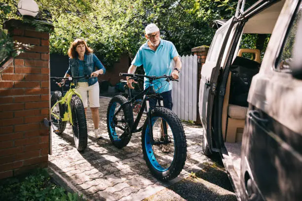 Senior couple works together to load their fatbikes into the waiting embrace of their campervan, preparing for a journey filled with adventure