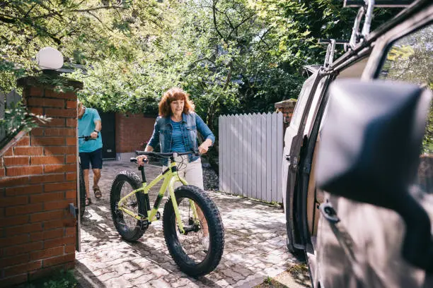 Senior couple, each with a fatbike in hand, strategically loads their bikes into the campervan, ready to roll into the next chapter of their journey together.