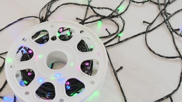 Garland sparkling with multi-colored lights on a black cable wound on a white reel lies on a light floor