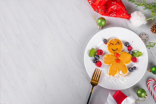Funny Christmas breakfast pancake in form of Christmas symbols - Christmas pudding, gingerbread man, Santa Claus' reindeer, with chocolate spread, berries, candy decor. Children holiday snack, brunch.