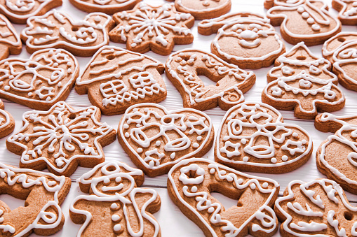 Gingerbread cookies of different shapes, decorated with icing on white wooden background.