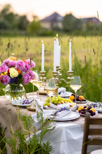 istock Summer sunset, romantic date outdoors in meadow, marriage proposal. Romantic sunset dinner in the field. Table honeymoon set for two with luxurious food, glasses of champagne drinks in a restaurant. 1805864115