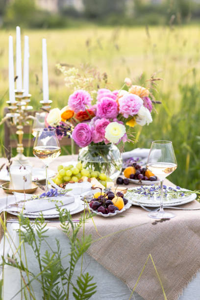 istock Summer sunset, romantic date outdoors in meadow, marriage proposal. Romantic sunset dinner in the field. Table honeymoon set for two with luxurious food, glasses of champagne drinks in a restaurant. 1805867695