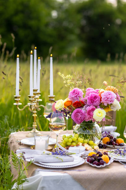 istock Summer sunset, romantic date outdoors in meadow, marriage proposal. Romantic sunset dinner in the field. Table honeymoon set for two with luxurious food, glasses of champagne drinks in a restaurant. 1805868334