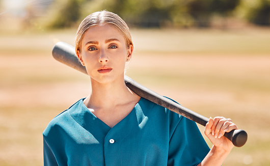 Baseball, sport and fitness with a sports woman ready for a game or match on a field or pitch outside. Exercise, training and workout with a young and healthy female athlete holding a bat outdoors
