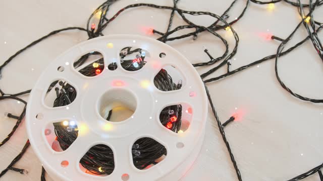 Reel with glowing multi-colored garland unwound with thread lies on white surface, glowing, ready decorate Christmas tree