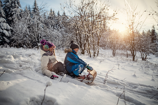Little boy and his elder sister are sledding with toboggan down little hill in the beautiful winter forest. Kids are 12 and 8 years old. They are enjoying the snow, the sun and the beauty of the winter.\nShot with Nikon D850