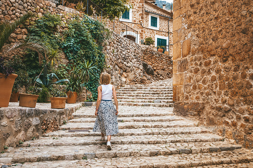 Woman going up the steps in the cozy street of a small village Fornalutx in Mallorca, Spain
