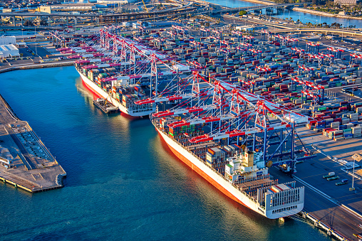 Aerial view of two large cargo ships moored in port at Long Beach, California being loaded with containers shot via helicopter from an altitude of about 800 feet.