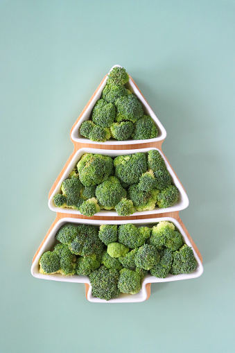Stock photo showing close-up view of Christmas party food buffet platter. Christmas tree shaped wood and china tray filled with broccoli florets displayed on a light green background.