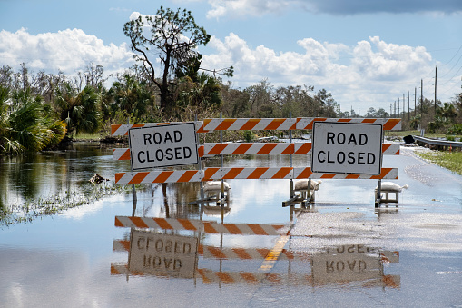 Flooded street in Florida after hurricane rainfall with road closed signs blocking driving of cars. Safety of transportation during natural disaster concept.