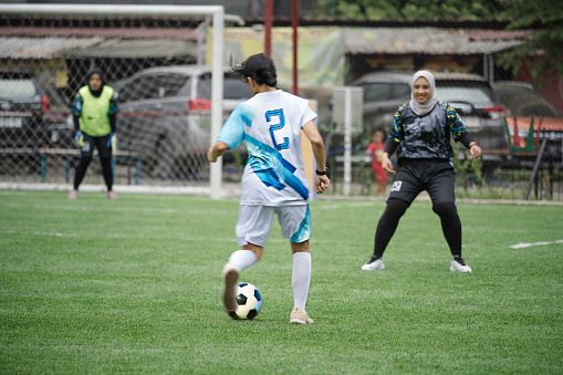 Offensive woman soccer player displays agility as she drives the ball across the field toward the opposing team's goal during a competitive game. The opposition chases after her.