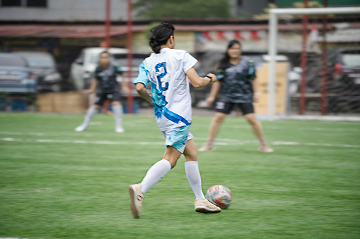 Offensive woman soccer player displays agility as she drives the ball across the field toward the opposing team's goal during a competitive game. The opposition chases after her.
