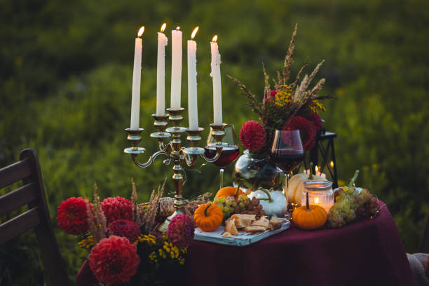 istock Beautiful decorated candlelight fall dinner, covered with a red tablecloth with flowers, pumpkins, candles, wine glasses. Outdoor in field near the forest in nature. Wedding banquet, sunset, evening 1805958439