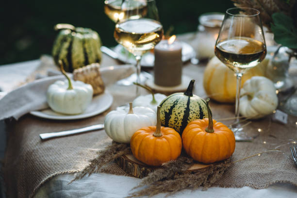 Beautiful decorated candlelight fall dinner, covered with a red tablecloth with flowers, pumpkins, candles, wine glasses. Outdoor in field near the forest in nature. Wedding banquet, sunset, evening
