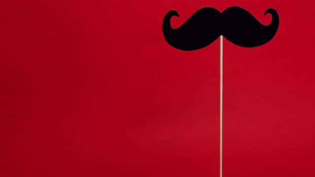A black mustache isolated on red background top view, copy space