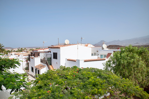 Costa del Silencio, Tenerife, Canary Islands, Spain - August 14, 2023: hot day above the rooftops of a picturesque residence with white villas built in Mediterranean style and surrounded by lush flora.