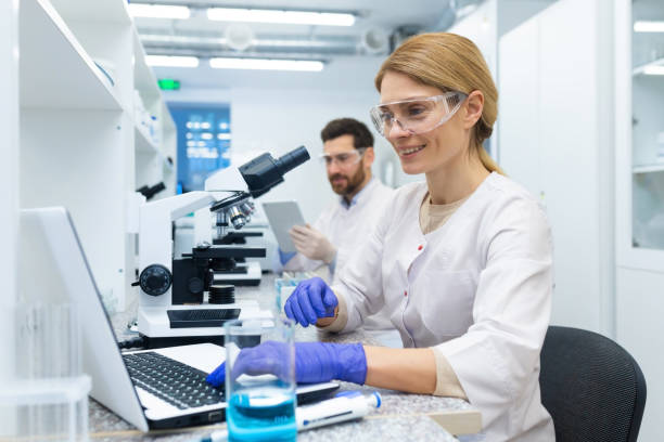 istock Mature female scientist in white coat at work, laboratory assistant using microscope and laptop at work, scientist working inside laboratory researching 1805989977