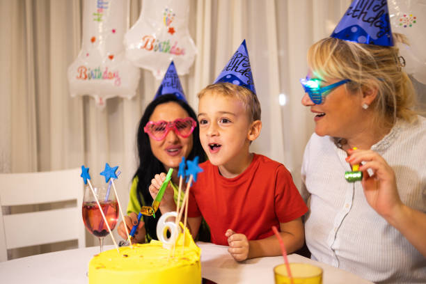 niño caucásico soplando vela en su pastel de cumpleaños, mientras celebraba su 6º cumpleaños con sus madres - ahijado fotografías e imágenes de stock