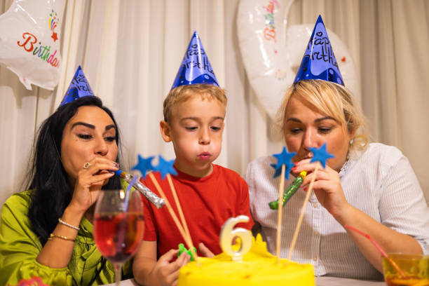 niño caucásico soplando vela en su pastel de cumpleaños, mientras celebraba su 6º cumpleaños con sus madres - ahijado fotografías e imágenes de stock