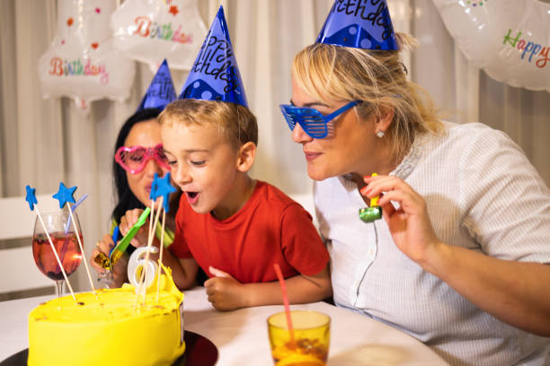 adorable niño caucásico soplando vela en su pastel de cumpleaños, mientras celebraba el 6º cumpleaños con sus madres - ahijado fotografías e imágenes de stock