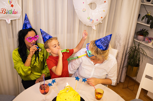 Excited Caucasian boy, celebrating his 6th birthday with his mother and nanny or godmother