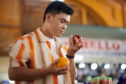 Young Vietnamese man buying fresh fruits like apples and oranges at market