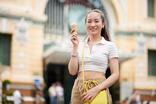 Portrait of happy young woman eating ice-cream when walking in city