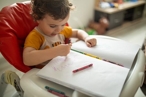 Toddler holding crayons and having fun with coloring at home