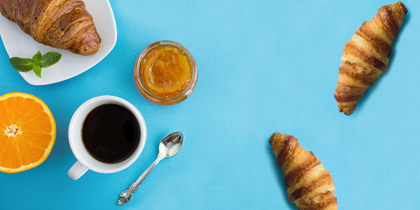 Continental breakfast with coffee, orange marmalade and croissant on the blue background. Top view. Copy space.