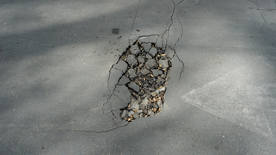 The road asphalt is cracked and destroyed with holes